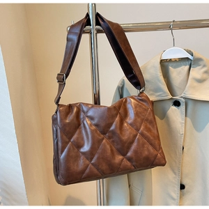 Close-up of quilted dark brown crossbody bag with wide shoulder strap and metal buckle