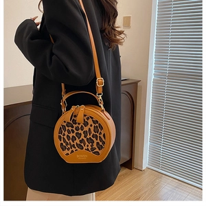 Detail view of round leopard print crossbody bag with dual zippers and leather handle