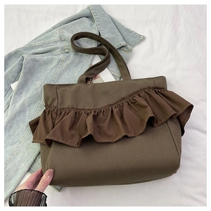 Close-up of brown canvas tote bag featuring ruffled trim and long shoulder straps on denim