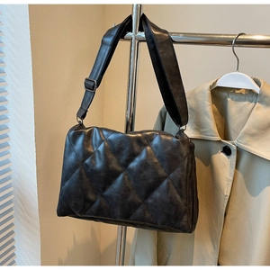 Detail of black quilted crossbody bag with adjustable wide strap and soft texture finish