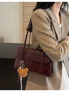 Vintage burgundy leather shoulder bag with plush bear charm on a model in a khaki blazer