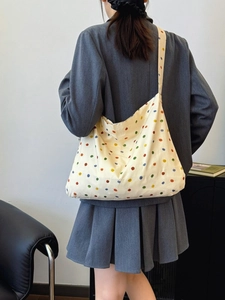 Beige canvas tote bag with colorful polka dots worn by a model in a gray suit