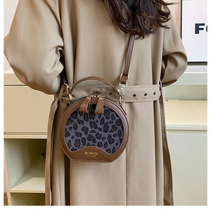Detail of round leopard print crossbody bag with brown leather trim and logo