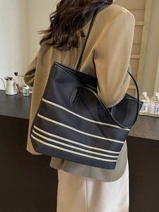 Black striped canvas tote bag with leather straps shown on shoulder for daily commute