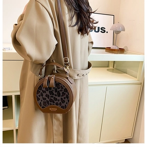 Brown faux leather round crossbody bag with leopard print accent shown on a model