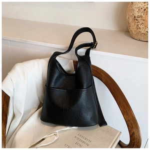 Detail of black matte leather bucket bag with front crescent pocket on a wooden chair