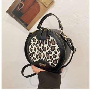 Detail of round black handbag with leopard print panel and golden dual zippers