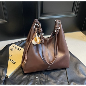 Detail of coffee brown tote bag with knot handle and baseball charm on leather jacket