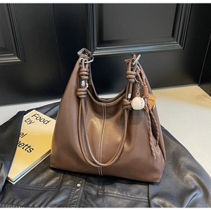 Detail of vintage brown tote bag featuring white stitching and baseball charm on leather