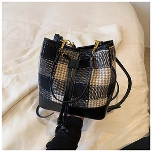 Détail d'un sac seau en tweed à carreaux avec base en cuir et fermetures dorées