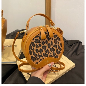 Detail of round leopard print crossbody bag with dual zippers and leather handle