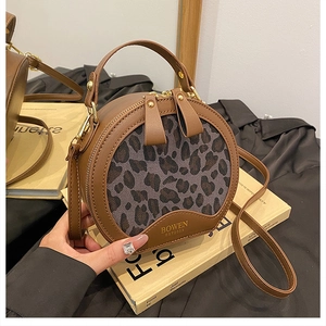 Detail of round leopard print crossbody bag with dual zippers and leather handle