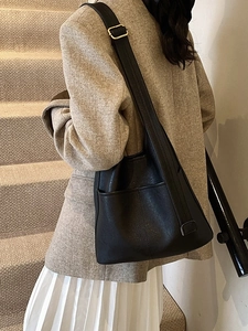 Minimalist black leather bucket bag with adjustable strap worn on a gray suit
