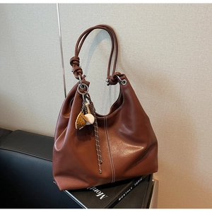 Detail of vintage brown leather tote bag with unique knotted handles and sports charm
