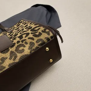 Detail view of leopard print tote bag base with gold metal feet and brown leather trim