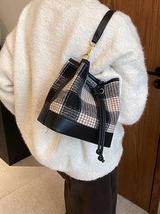 Sac seau en tissu pied-de-poule et cuir porté par un mannequin avec bandoulière