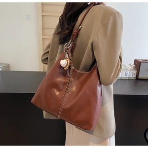 Detail of dark brown tote bag with white contrast stitching and baseball pendant