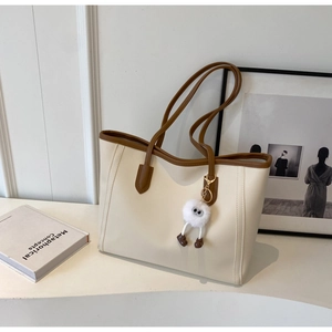 Close-up of cream tote bag with contrast brown straps and a cute plush doll charm