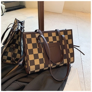 Detail of checkered canvas tote bag with brown leather trim and twin handles