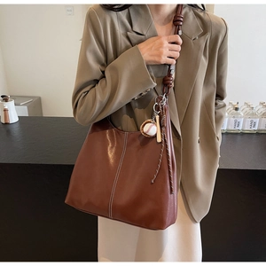 Detail of vintage brown tote bag with white stitching and baseball charm on a model