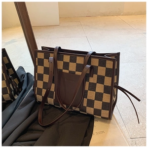 Detail of checkered tote bag with brown leather pocket and adjustable side drawstrings