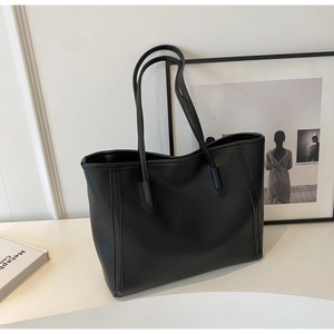 Detail of minimalist black leather tote bag featuring long handles and precise stitching