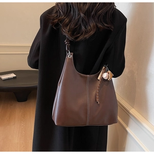 Detail of dark brown leather hobo bag with contrast stitching and baseball charm