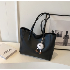 Detail view of black matte tote bag with fuzzy white monster charm and long strap