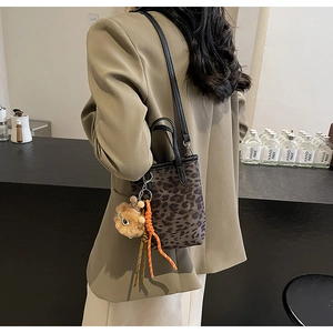 Détail du sac seau léopard avec charm en peluche et bandoulière en cuir noir