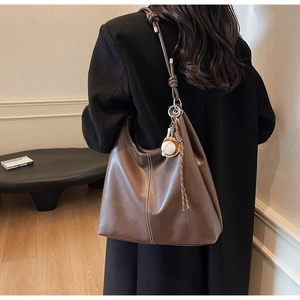 Detail of dark brown leather tote bag featuring baseball pendant and knotted shoulder strap