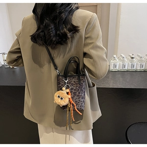 Détail du sac seau à imprimé léopard avec pendentif en peluche et sangle tressée orange