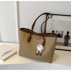 Detail of khaki tote bag with plush charm on minimalist white display stand