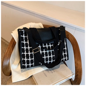 Detail of checkered tote bag with leather trim on a wooden chair in a minimalist setting