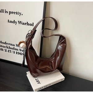 Detail of dark brown glossy crescent bag with baseball charm on white books