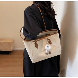 Detailed side view of large off-white tote bag with brown trim and plush monster charm