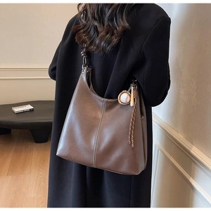 Detail of dark brown leather tote bag with white contrast stitching and baseball charm