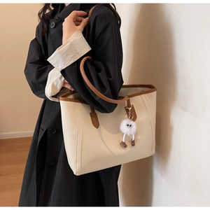Detail of off-white tote bag with brown leather trim and a cute plush ball charm