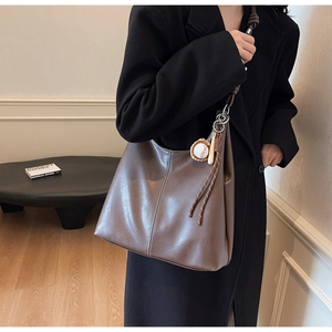 Detail of dark brown leather tote with white stitching and baseball charm on shoulder