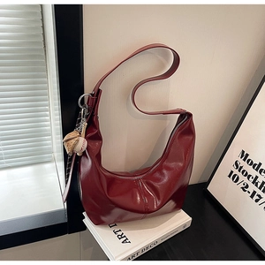 Detail of dark red crescent hobo bag with glossy finish and baseball charm decoration