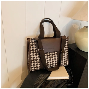 Detail of houndstooth fabric and brown leather handle on large tote bag with brand logo