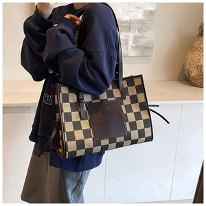 Detail of checkered tote bag with brown leather front pocket and sturdy handle strap