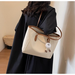 Detail of minimalist tote bag in cream and brown with a cute plush monster charm accessory