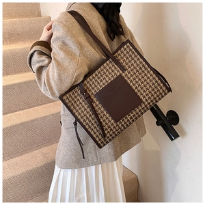 Detailed view of the houndstooth fabric texture and brown leather trim on a tote bag