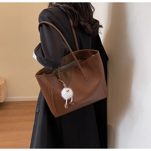Detail of minimalist brown faux leather tote bag with a white plush monster charm
