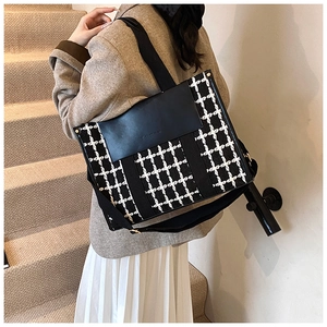 Detail of checkered tote bag with black leather flap and wide strap worn by a model