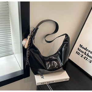 Detail of glossy black hobo bag with baseball charm on white books in minimalist setting