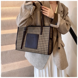 Detail of classic houndstooth tote bag with brown leather trim and embossed branding