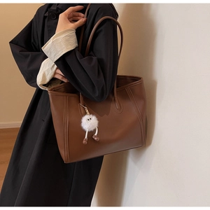 Brown leather tote bag featuring a white fuzzy monster charm for large capacity commuting