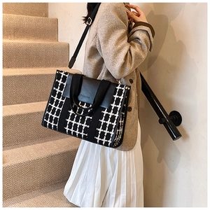 Detail of checkered tote bag with black leather flap and golden hardware accents