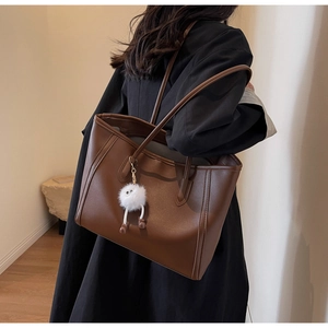 Detail of a large brown tote bag with white plush charm worn on shoulder